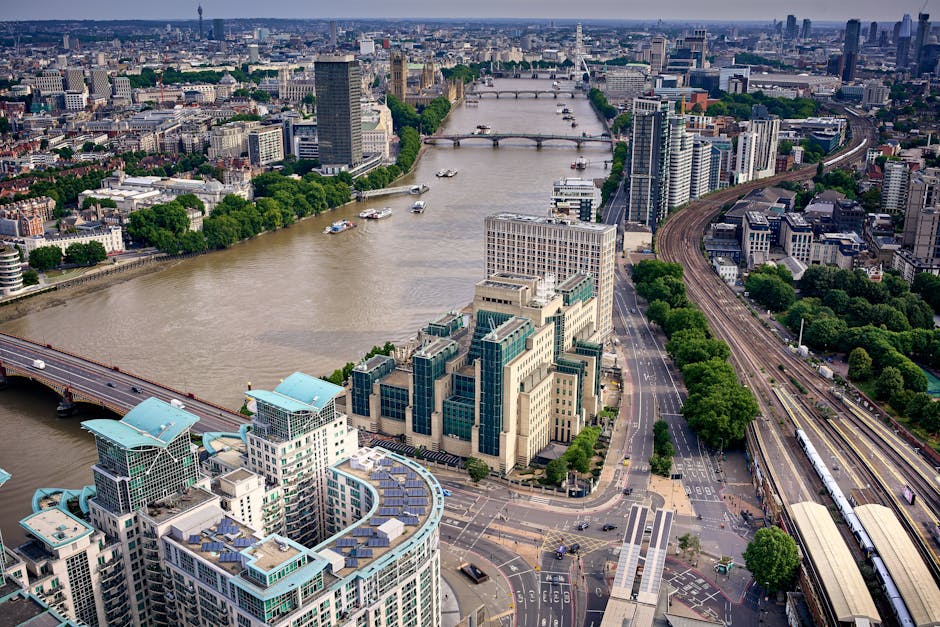 A wide-angle view of a cityscape at sunset showing modern residential buildings with distinctive architectural features, situated along a river. The buildings are illuminated by the warm light of the